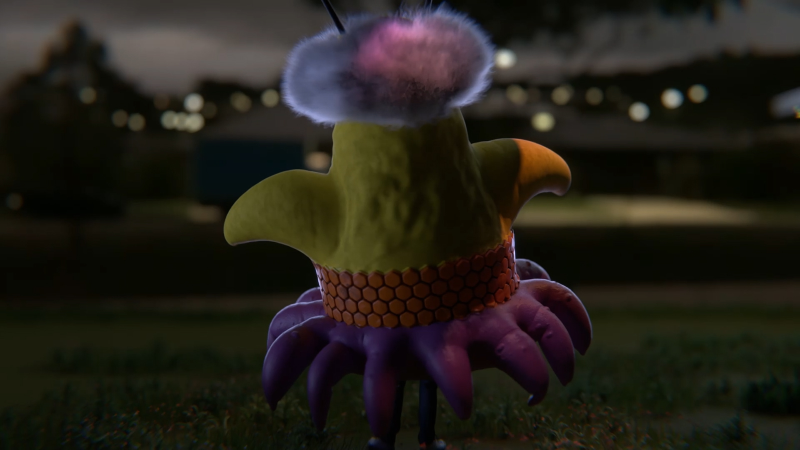 A colorful creature stands outdoors at night, viewed from behind. It has a rounded yellow body with small outstretched arms, a purple skirt-like base with petal shapes, and a fuzzy pom-pom on top of its head. Blurred city lights glow in the background.