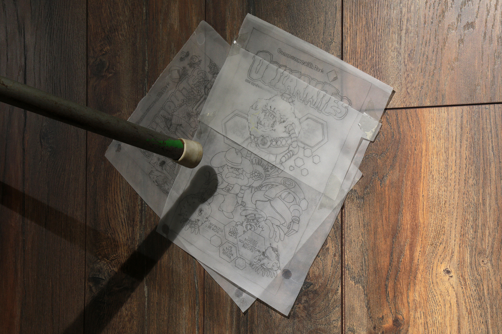 pencil drawings on tracing paper copied from a comic book are stuck to a wall covered in wooden floorboards.  A chair leg from an old school chair points to the drawings.